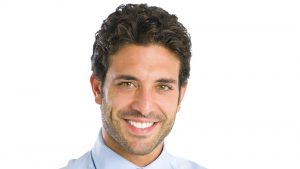 Foto de homem branco de cabelos castanhos sorrindo para ilustrar conteúdo de cirurgia de calvície.